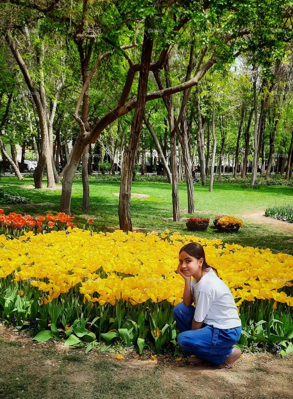 Cute girl with her pure smile has joined the warm crowd of green stems , support of the trees and is gradually drowning in colourful tulips