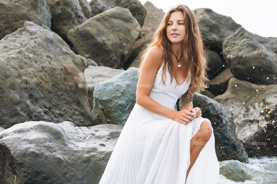 Young carefree beautiful woman with long hair in white dress enjoying life on sea beach