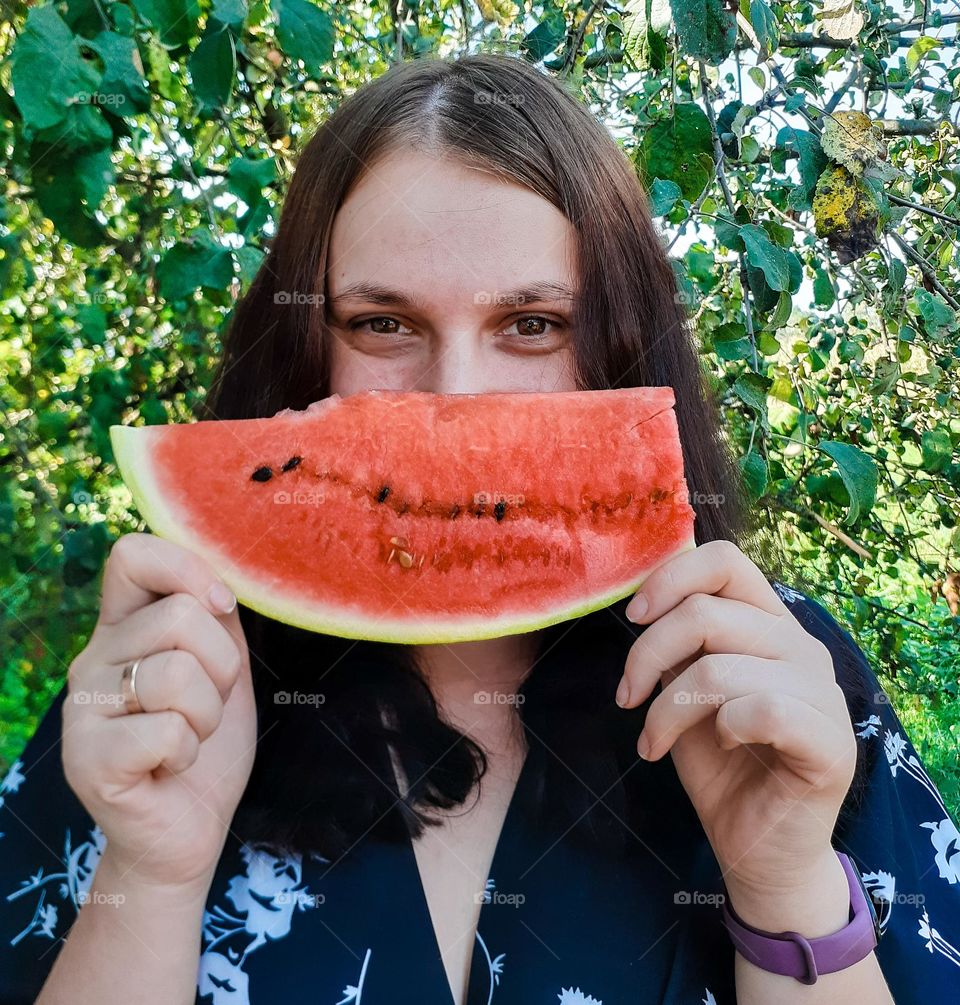 The girl enjoys a large piece of fresh watermelon in city park