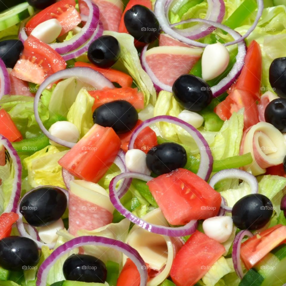 Antipasto salad of lettuce, tomatoes, black olives, red onions rings, garlic, salami, provolone and mozzarella cheese, and green peppers