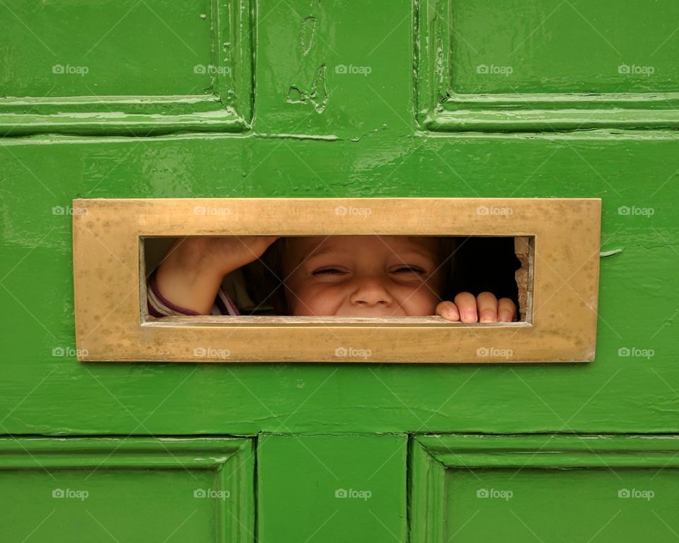 Child looking through the letterbox of a green front door
