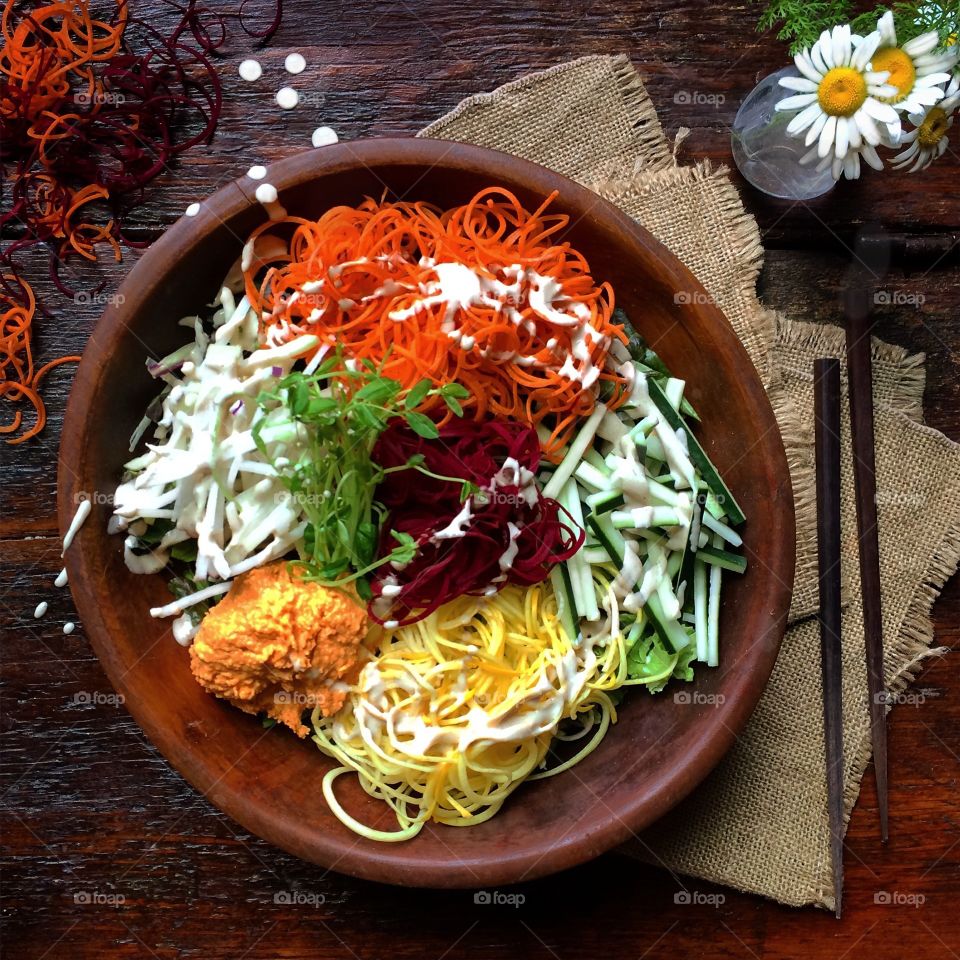 Colorful salad bowl with spiraled vegetables in a wooden bowl next to chopsticks.