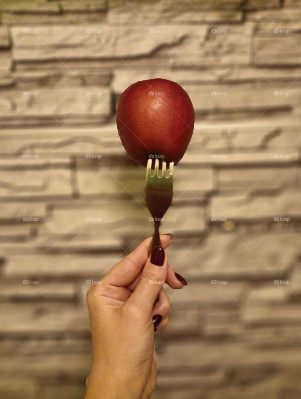 fork, apple, apple on the fork, water drops, the fork pierced the apple, a female hand holds a fork, 
red apple, stone wall, color photography