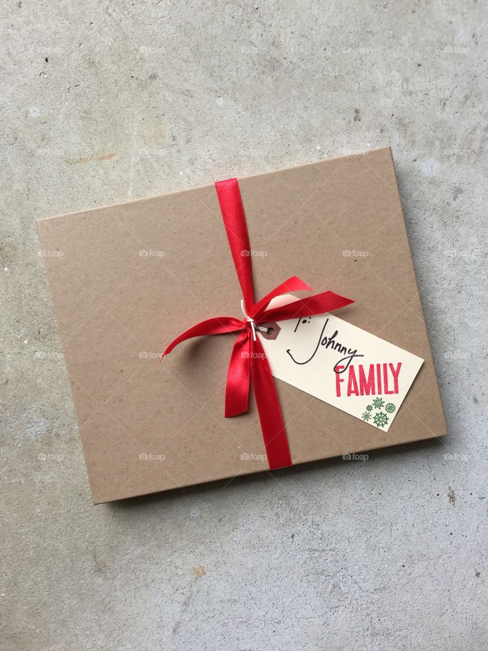 Brown rectangular craft cardboard gift box tied with single red festive ribbon and gift tag with handwriting family 