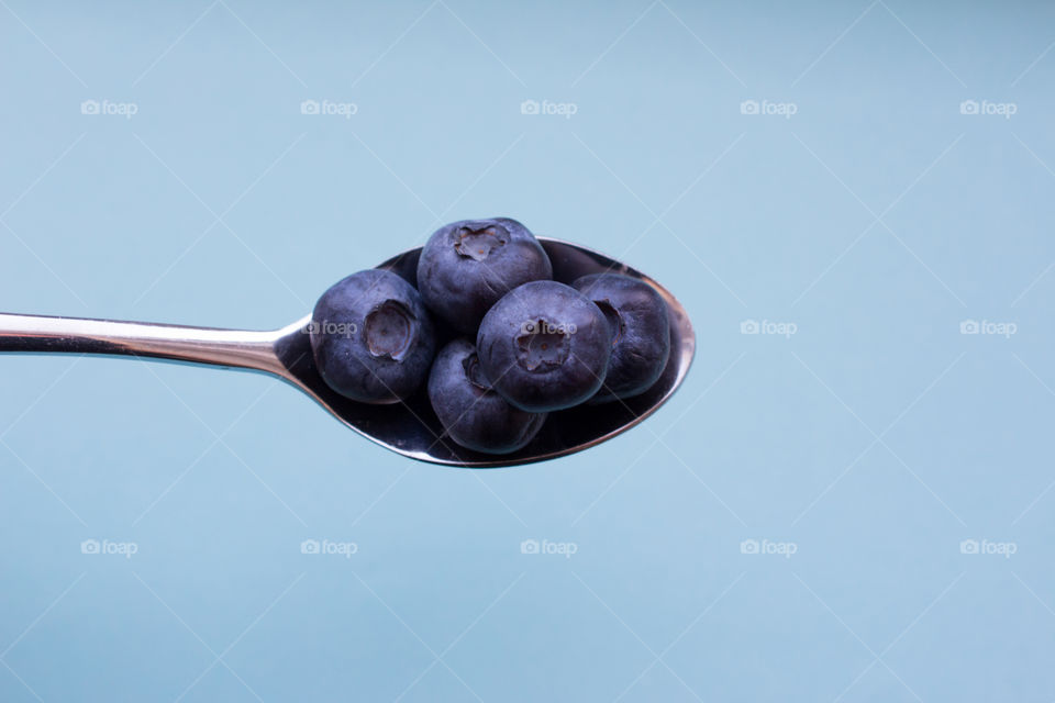 A spoon filled with blueberries , blue background 