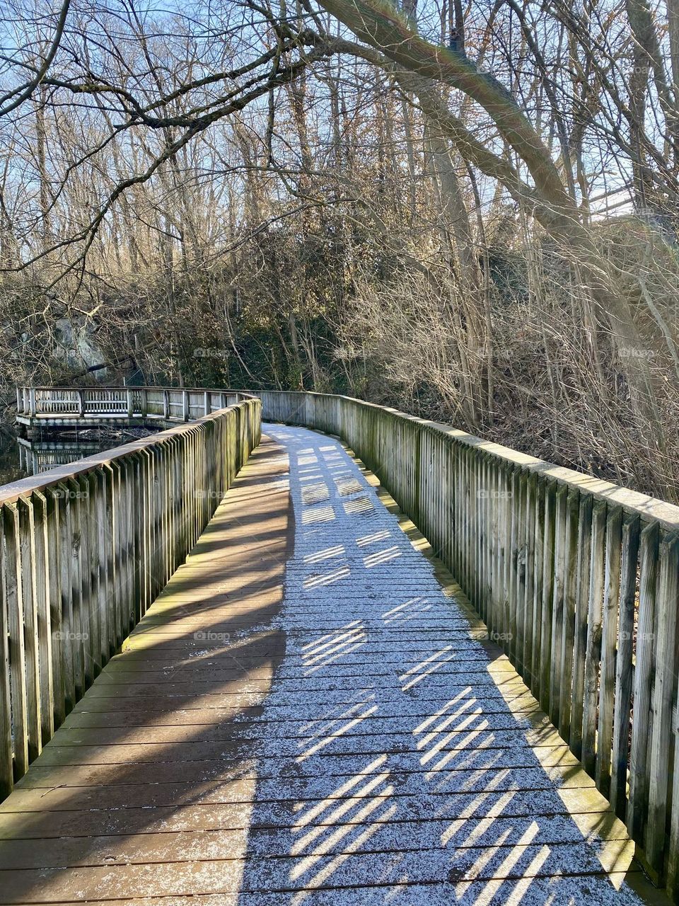 Snow and shadows on a boardwalk around a quarry lake at a local park 