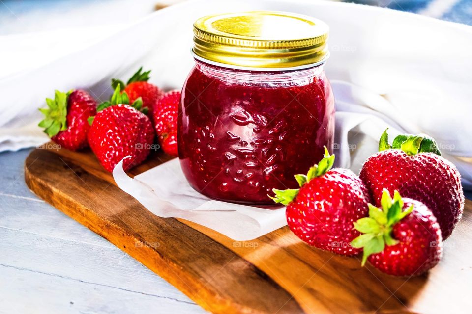 Fresh strawberry jam placed on a wooden chopping board, surrounded by strawberries.