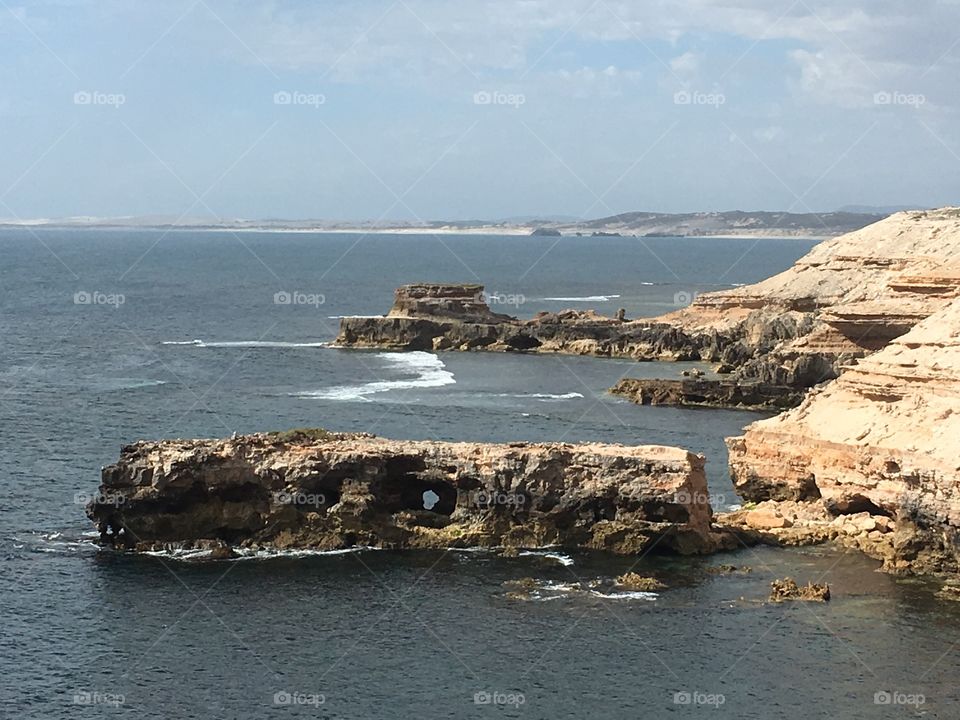 View of large rock in ocean with hole through it, from high atop an ocean cliff