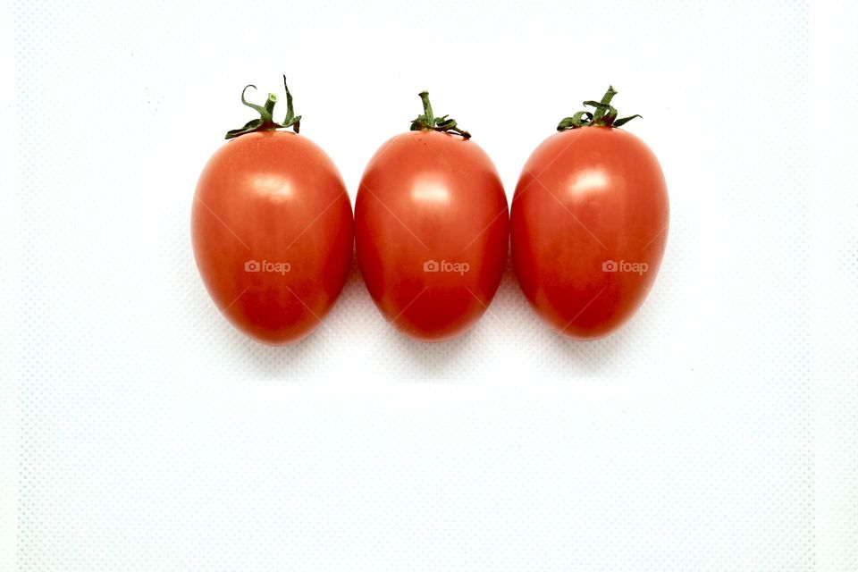 Small organic red ripe Roma tomatoes,assembled in a group symmetrical row of three, isolated on white background with room for copy text; food and nutrition, teamwork, health and diet 