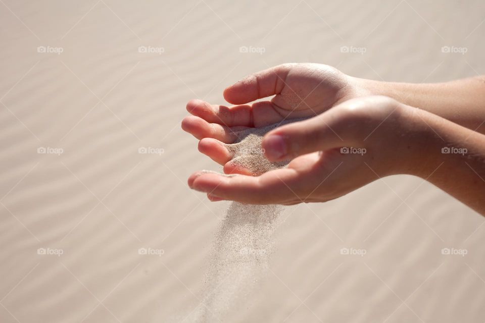 Close-up hand releasing dropping sand. Sand flowing through the hands against sunny beach sand.