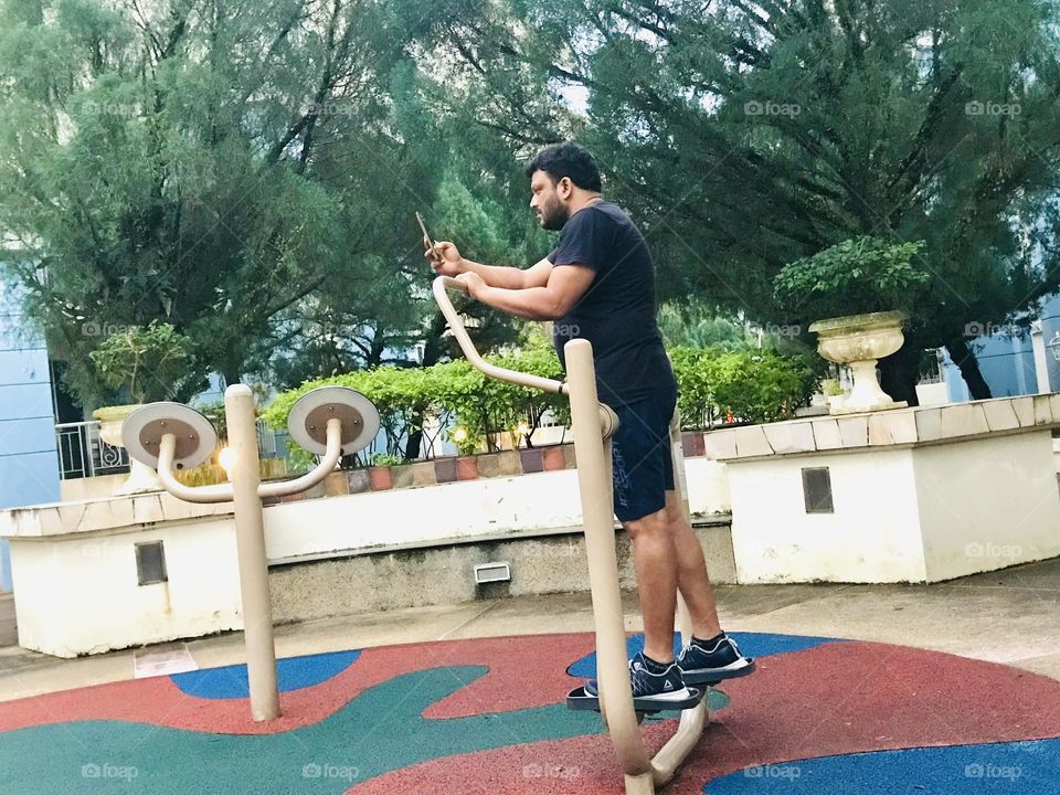 Man looking phone while doing exercise at outdoor gym