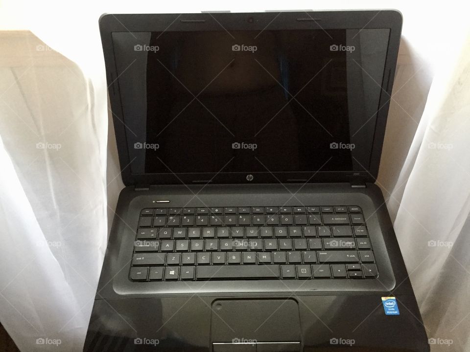 A black laptop computer in front of a window with white sheer curtains