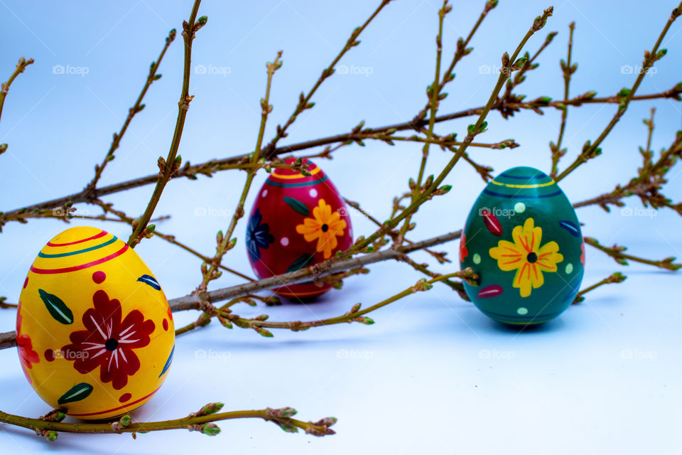 Three colorful wooden Easter eggs hidden within blooming spring branches