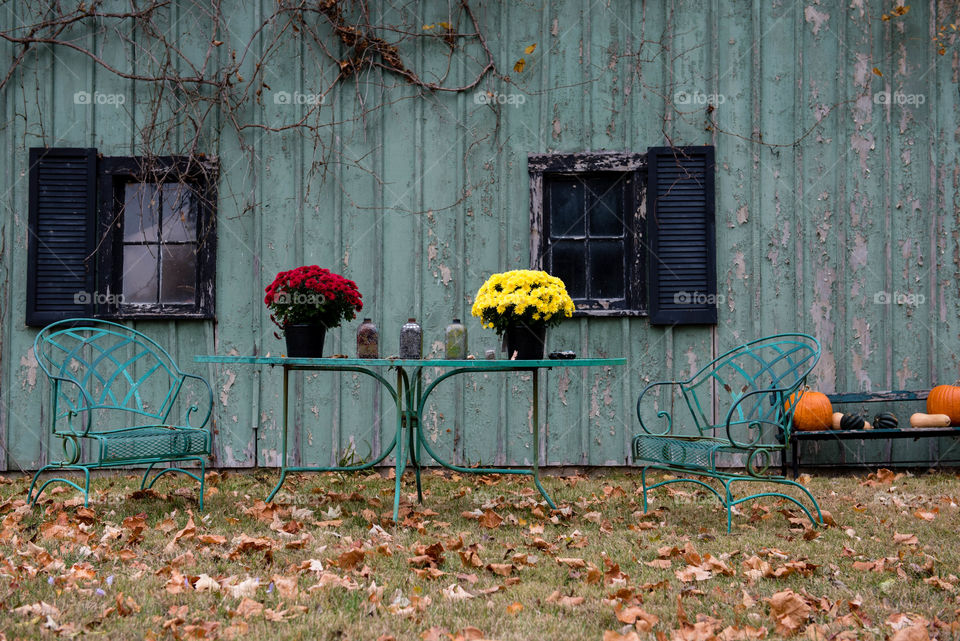 Wrought iron table and chairs sitting outdoors amongst fall leaves in front of a rustic barn