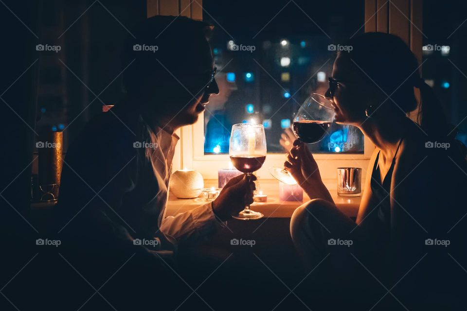 Couple having romantic dinner drinking wine at home. Night city lights on background 