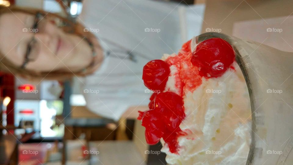 milkshake with cherry on top of whipped cream with figure in background