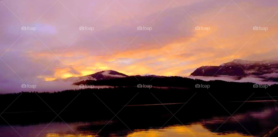 fog misting the the mountains with the sunset reflections in the water.