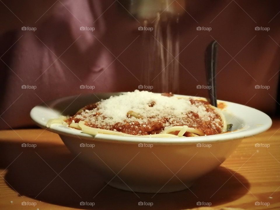 Girl sprinkling her Italian tomato sauce spaghetti with powdered dry parmesan cheese in her plate bowl with fork in the plate in a dark atmosphere with lights and shadows effects and time in motion, long exposure.