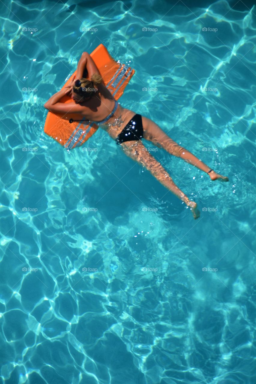 A young lady enjoys floating in a cool blue refreshing swimming pool. 