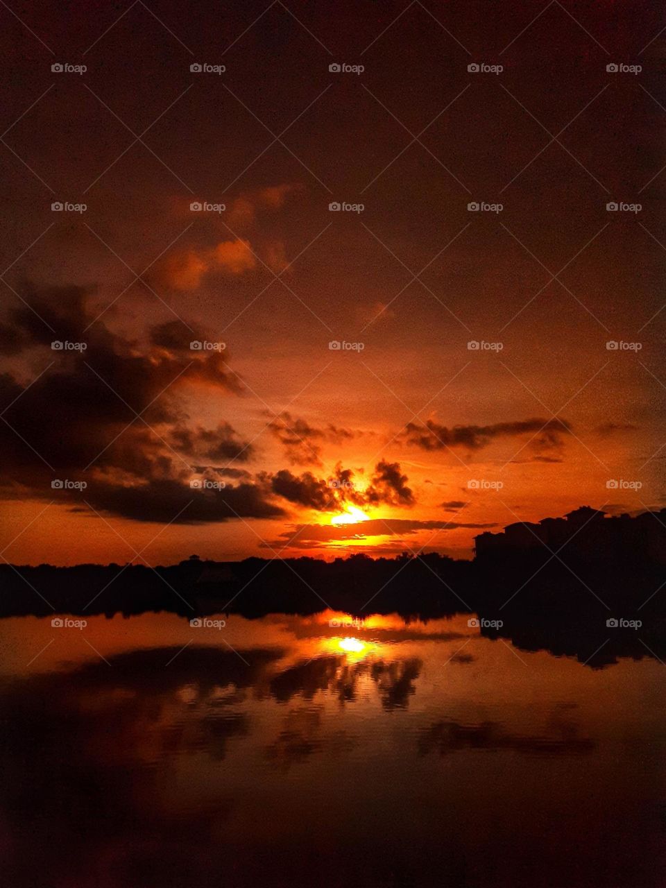 A reddish orange sunrise through dark clouds over the lake at Cranes Roost Park in Altamonte Springs, Florida.