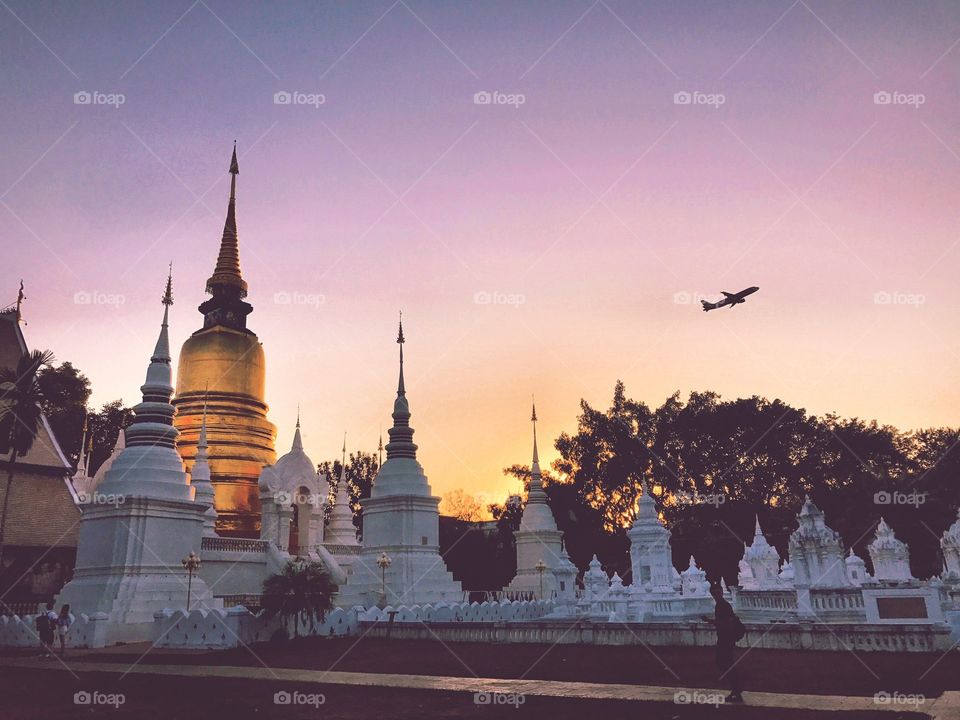 Buddhist temple in Chiang Mai, Thailand, with airplane taking off from runway during sunset