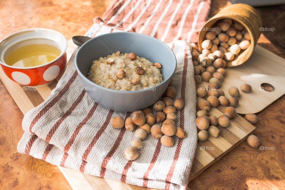 Cooked oatmeal in a deep gray plate with hazelnuts and honey.