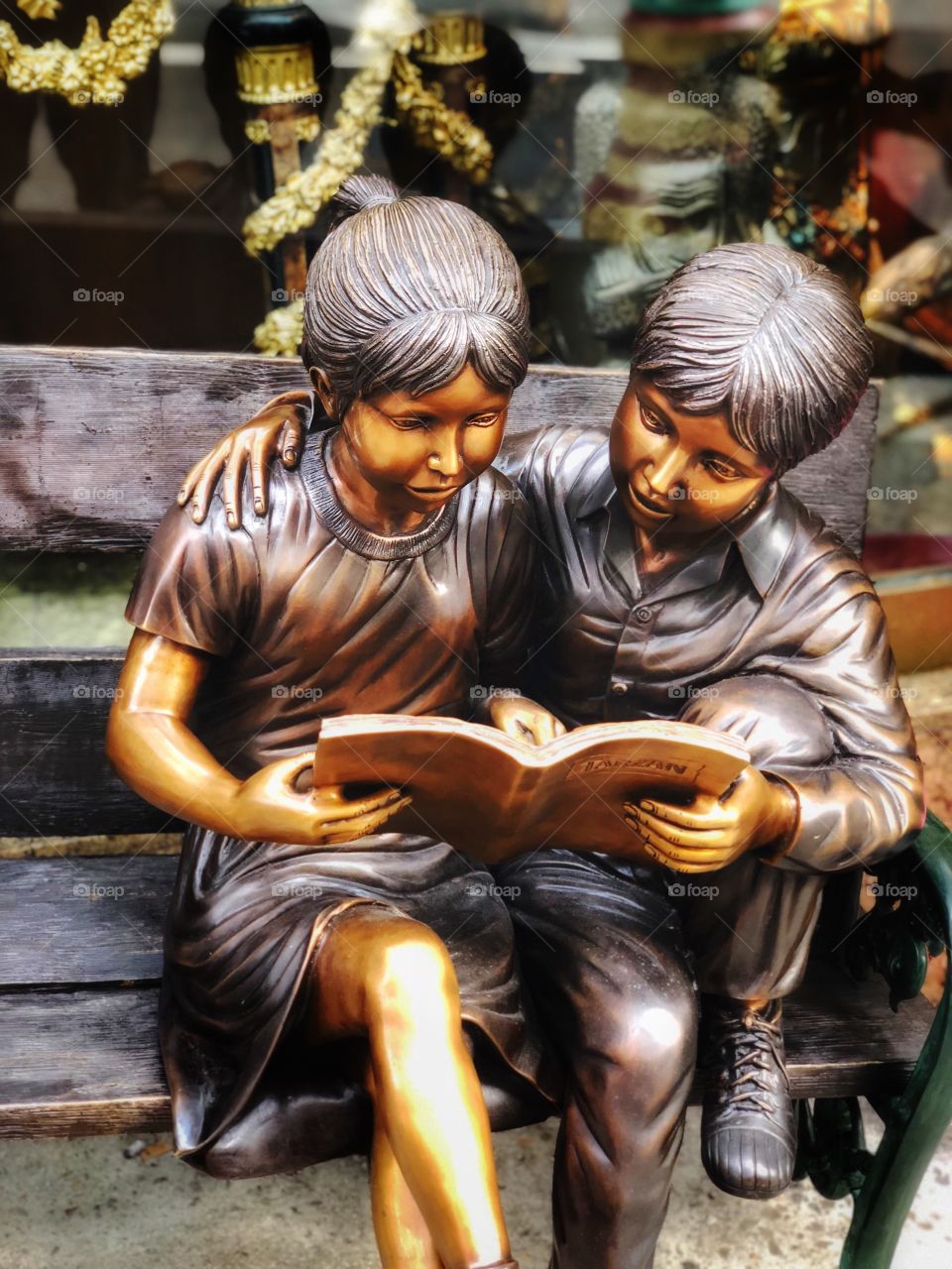 A metal statue with 2 kids reading a book on a bench.