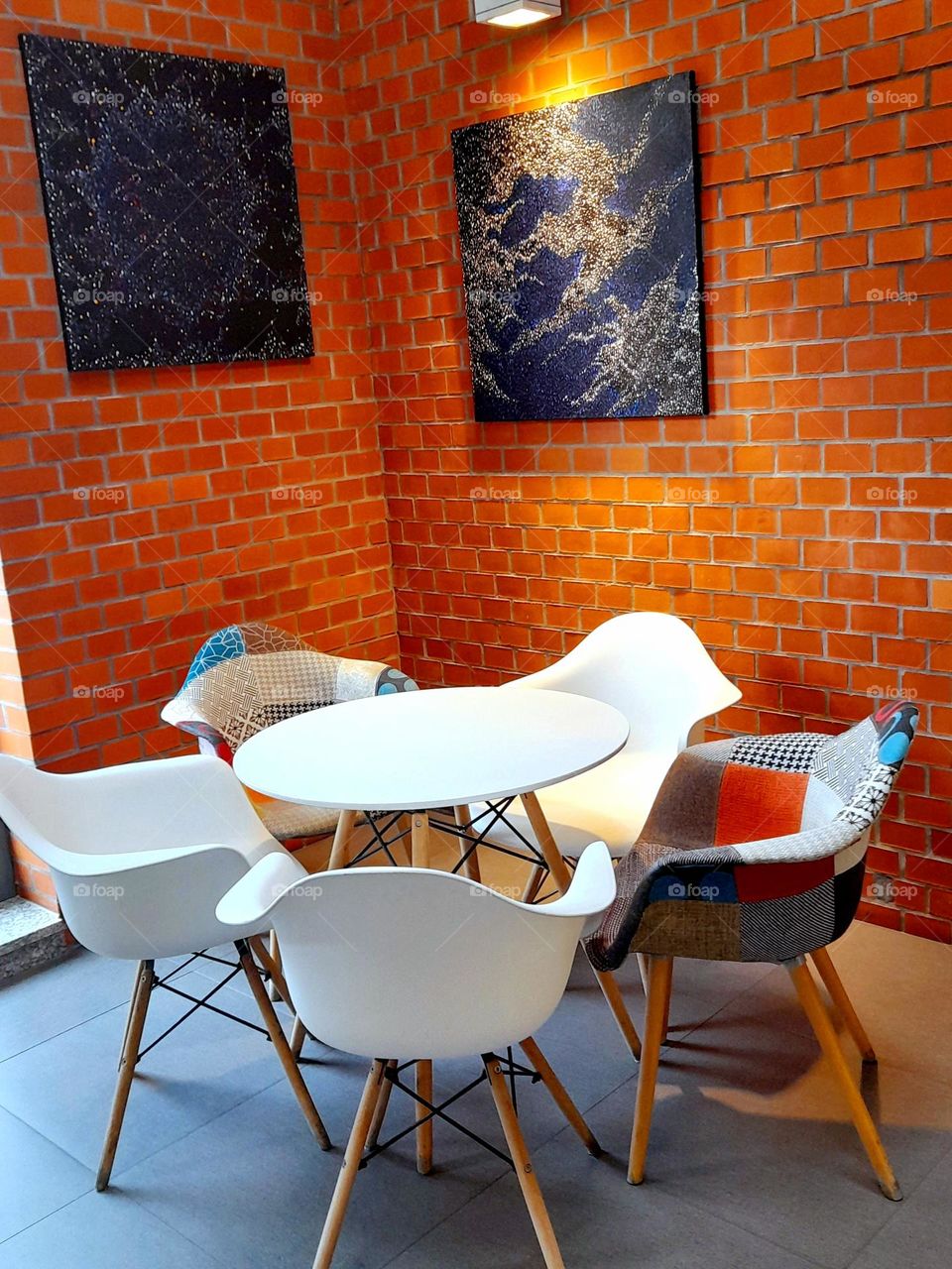 White table with white and colorful chairs standing against a brick wall.