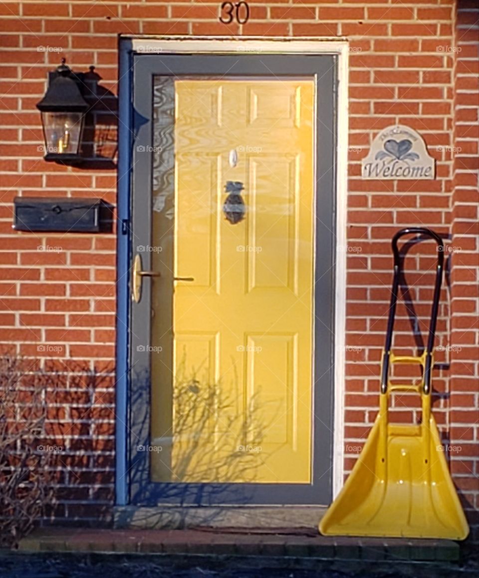 Yellow door with pineapple knocker yellow shovel against brick house