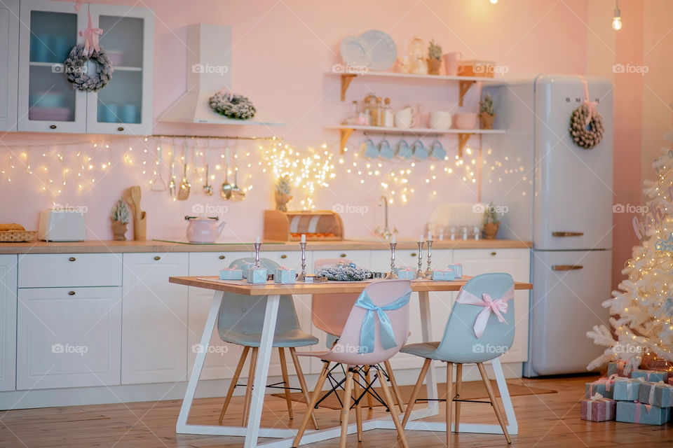 Festive winter cozy kitchen interior with garlands, decorations and gifts.  Christmas dinner at the decorated table.