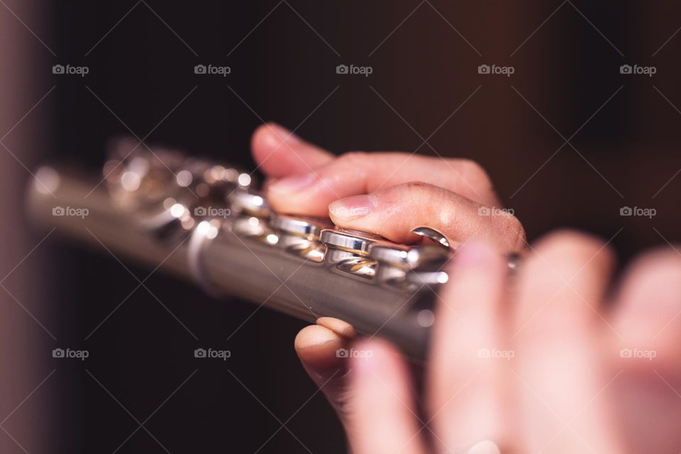 A portrait of the fingers of a flutist playing on a silver flute. the musician is pressing the valves.