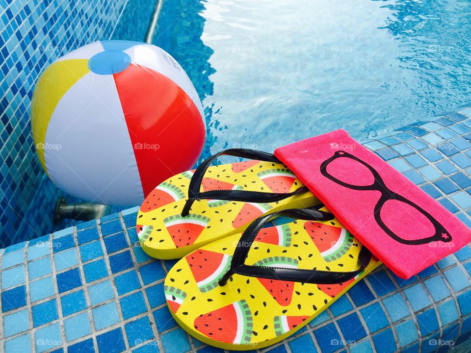 Flip flops with watermelons,pink sunglasses case and water ball near the pool