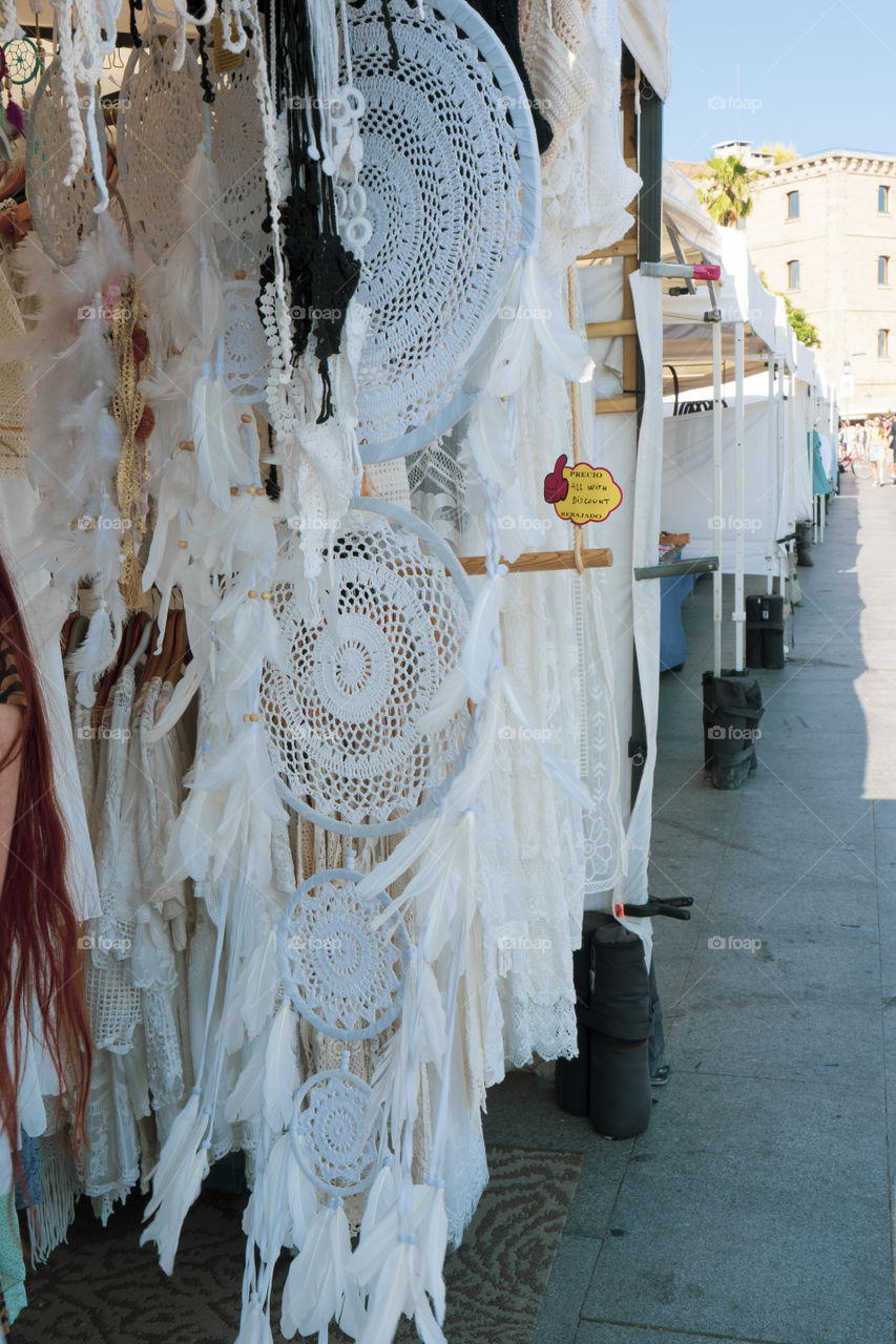 Clothes in a barcelona stall. You see a dream catcher. Everything is white and in theme.