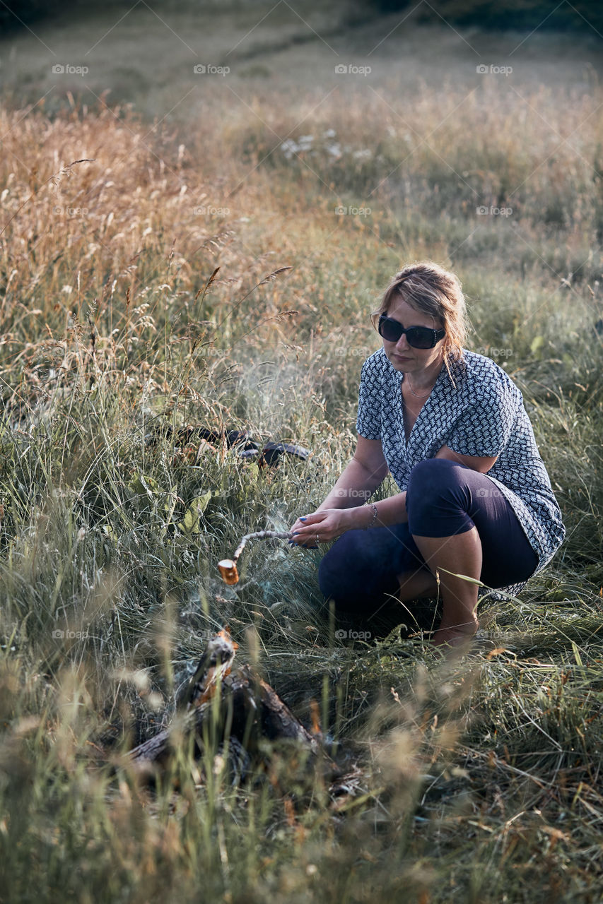 Woman roasting a marshmallow over a campfire on meadow. Vacations close to nature. Candid people, real moments, authentic situations