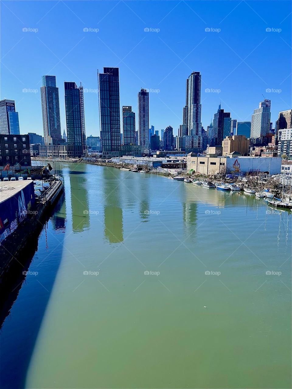 This is „Newtown Creek“ seen from the „Pulaski Bridge“ that connects LIC, Queens to „Greenpoint“, Brooklyn. Across the water we see „Greenpoint“ on the left then LIC and in the far distance „Manhattan“ on the right. 2024. Hypnotic Productions