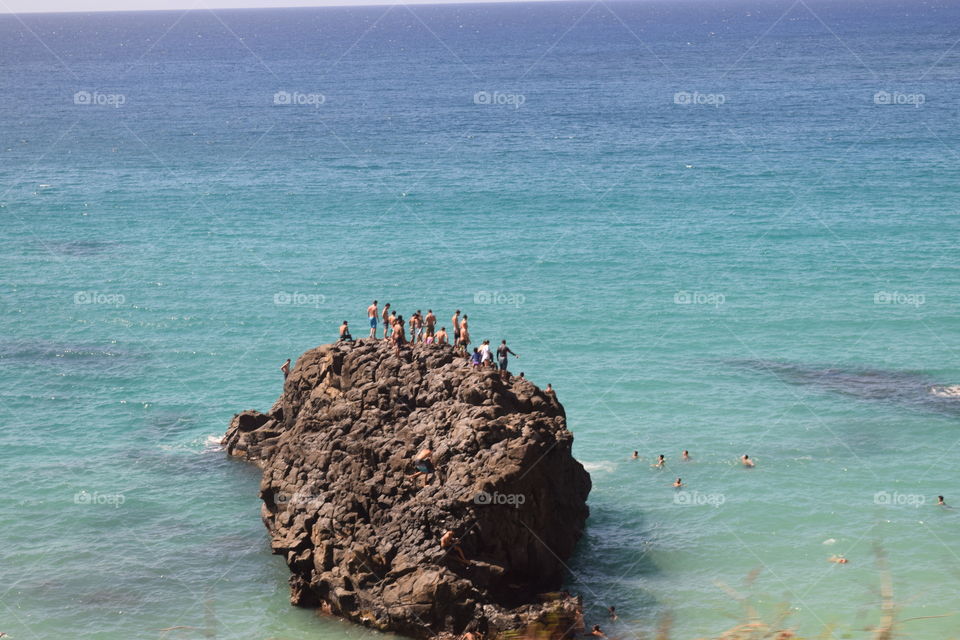 People jumping from a rock in Hawaii,  having fun in the clear blue water