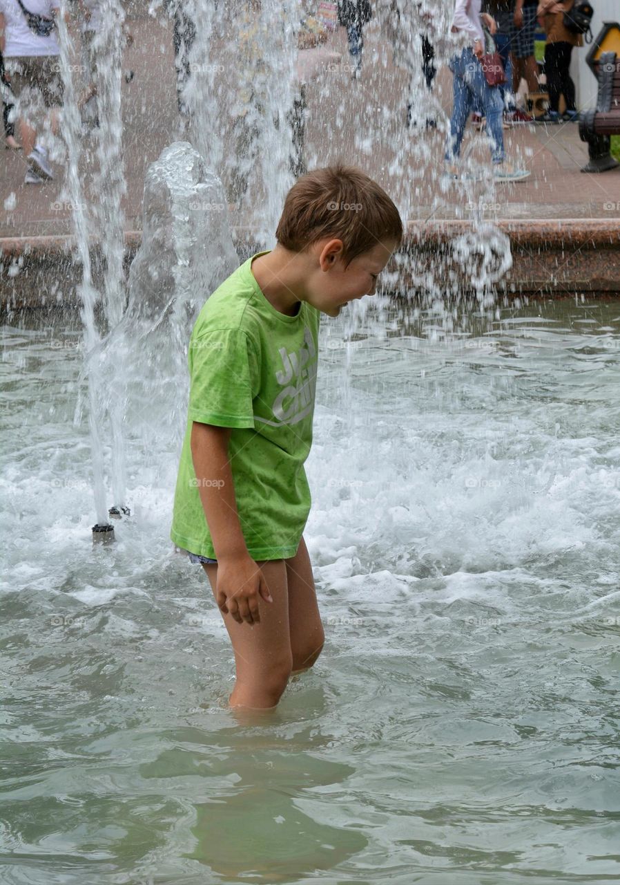 child boy in water fountain urban nature summer time