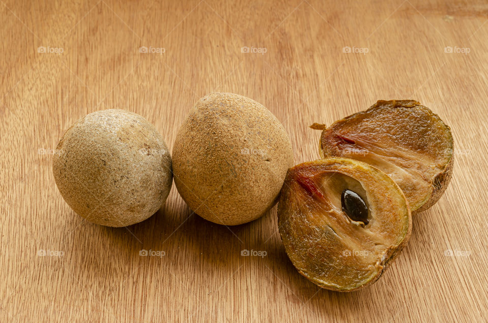 Ripe Sapodilla (Naseberry) fruits, whole and cut sitting on a board table with it black seed in a half.