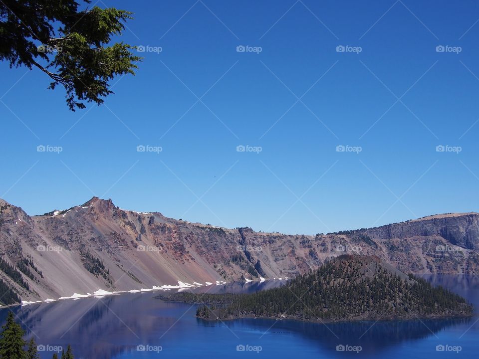 The jagged rim reflecting into the rich blue waters of Crater Lake in Southern Oregon on a beautiful summer morning with perfect clear blue skies. 