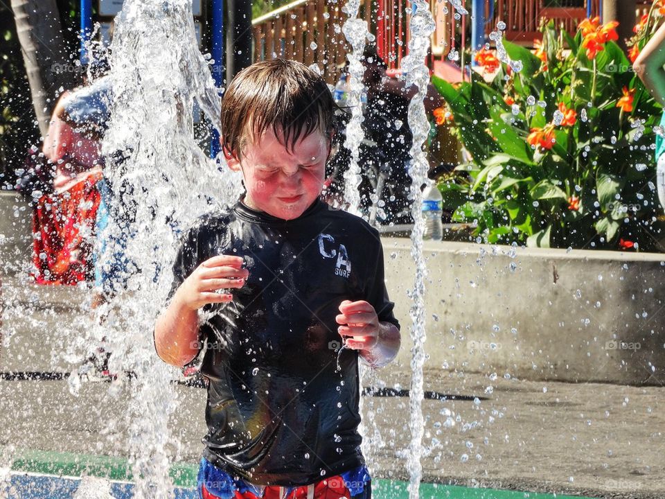 Boy Splashing In A Water Fountain. Beating The Heat In Summer