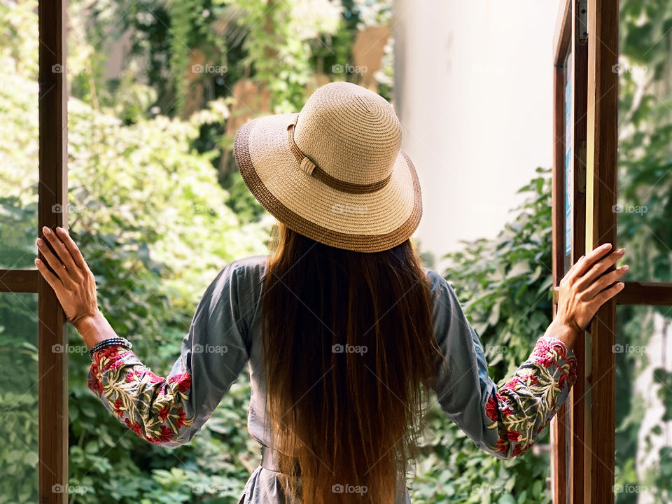 Young woman with long hair in hat at the opened window 