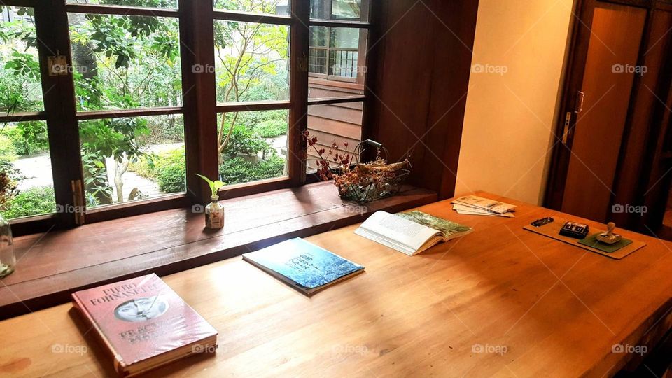 Books, wooden table, green plants outside the window