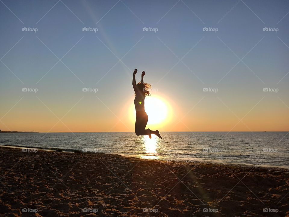 Bounce. Jumping girl at dawn on the seashore. Sunrises. Sunsets. The sun. Girl. Yoga by the sea. Sea. Silhouette. Sunlight.