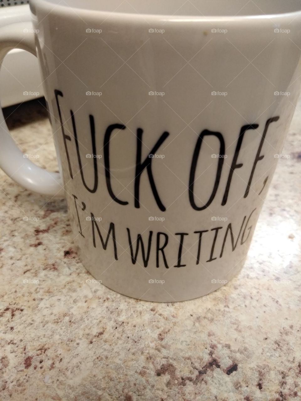 A white coffee mug that says "F*** off, I'm Writing" in black letters