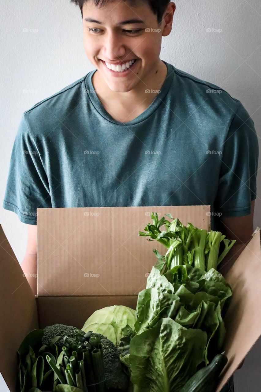 Happy healthy young man with a box of green vegetables