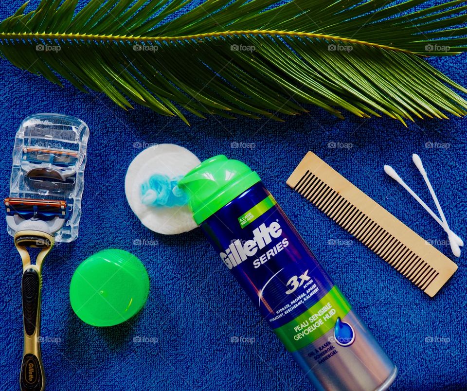 Gillette shaving cream and razor on a blue towel with comb and palm leaf.