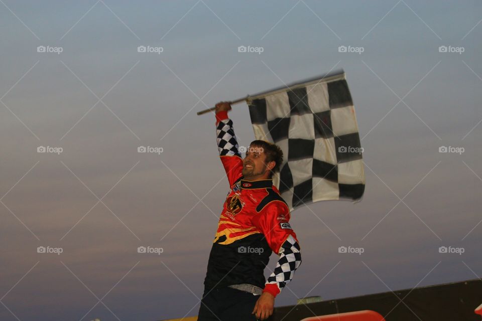 race car driver waving checkered flag in victory lan after winning a race 