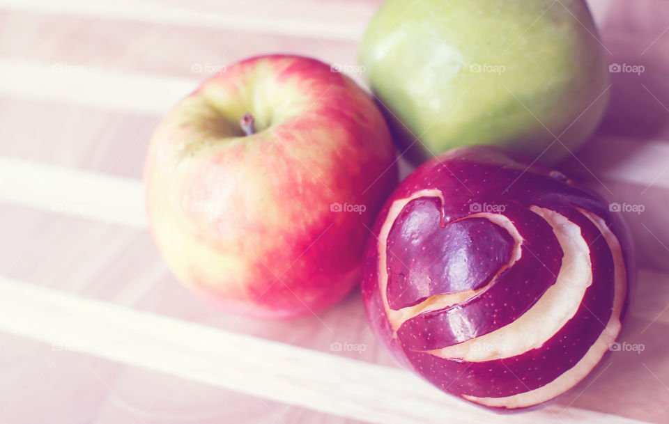 Shiny fresh apples on wood table background with heart shape design cut into deep red apple symbolic of love or healthy diet and nutritional choices for family snacks 