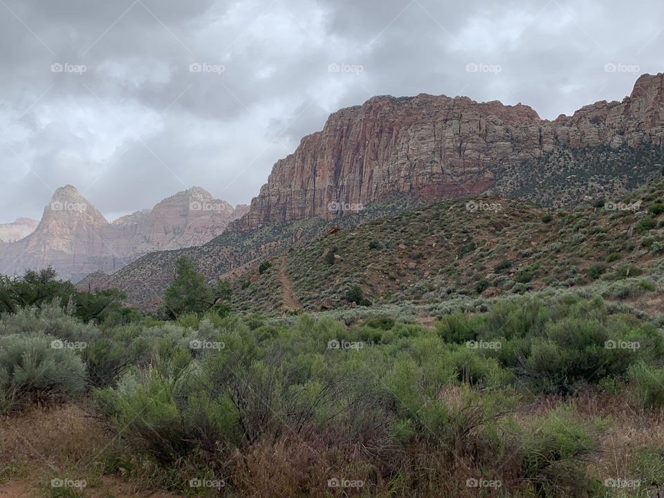 A red and tan cliff with clouds above.