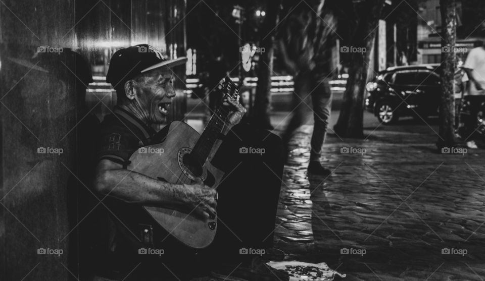 A blind street performer right beside Robinson's place, Fuente Osmeña, Cebu, Philippines. He sang his heart out while  people were partying right across the street.